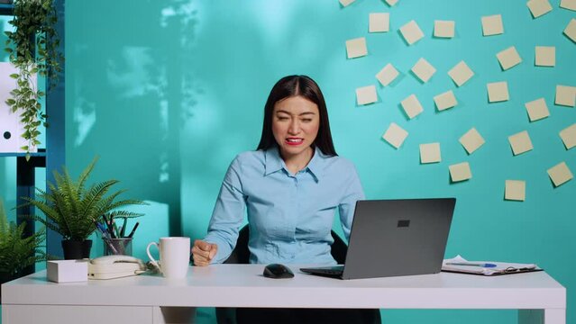 Angry emotional businesswoman screaming and slamming fists on table after reaching end of patience at work. Furious offended asian employee having impulsive gesture while at office desk