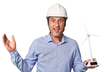A middle-aged architect man holding a windmill model receiving a pleasant surprise, excited and raising hands.