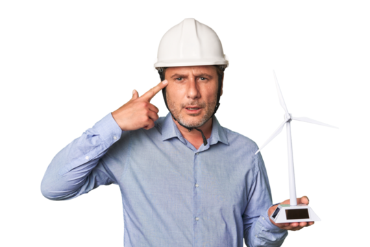 A middle-aged architect man holding a windmill model showing a disappointment gesture with forefinger.