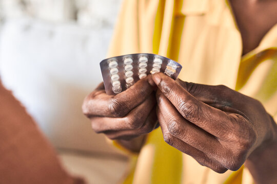 Seated on her sofa, an African woman takes her pills, continuing with her treatment.