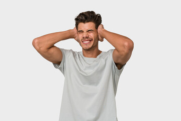 Young handsome caucasian man isolated on white background covering ears with hands.