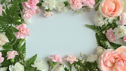 Frame made of pink rose, carnation and fern leaves on white background. Flat lay, top view with space for text