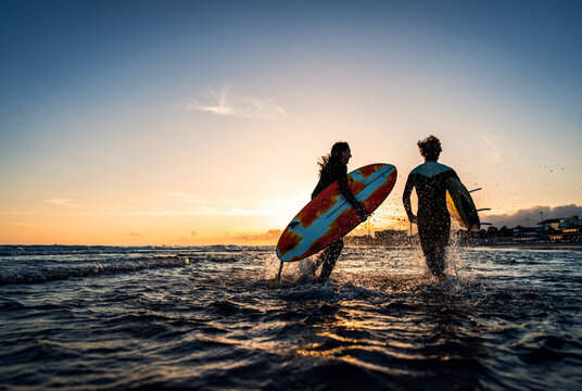 Two surfers with surfboard prepares to hit the waves at sunset.