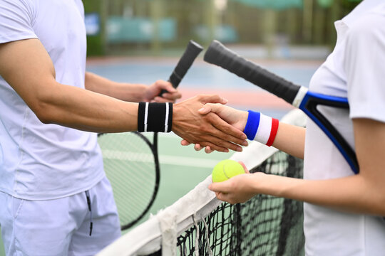 Male and female tennis players shaking hands over net at tennis court after the match. Good sportsmanship, friendship wins