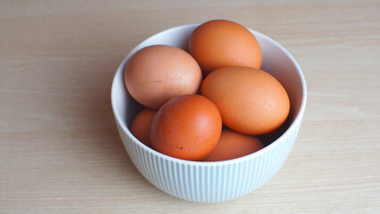 Fresh eggs in ceramic bowl on wooden table as a background with copy space