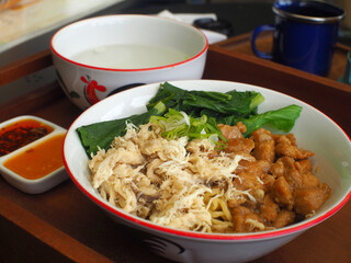 Asian chicken noodles complete set with soup and chili oil on a wooden tray.
