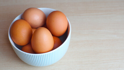 Fresh eggs in ceramic bowl on wooden table as a background with copy space