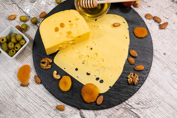 Maasdam cheese with dried apricots, nuts and honey on a graphite board. Top view.