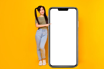 Full size photo of young pretty female recommend new social network app in huge phone isolated on yellow color background