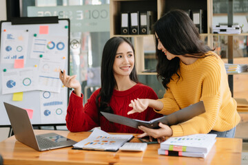 Two Asian businesswoman discuss investment project working and planning strategy with tablet laptop computer in office room.