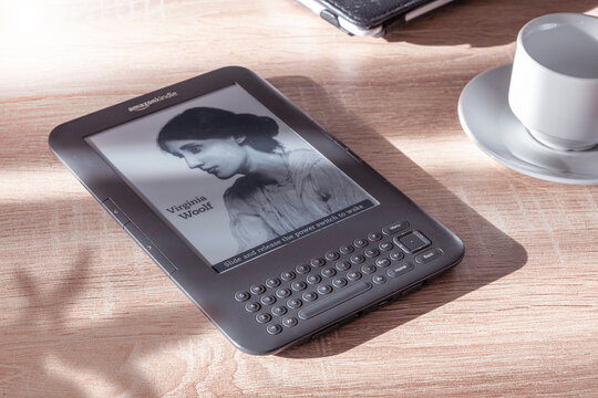 
Amazon Kindle ebook reader on a wooden table next to a plant and a cup of coffee. Empty copy space for Editor's text.