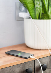 Smartphone being charged via USB cable connected to an electrical outlet, lying on a chest of...