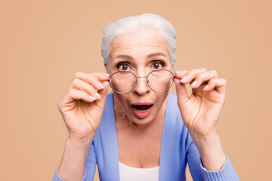 Discounts And Sales What A Great News Close Up Portrait Of Old Woman Looks Over Her Spectacles In Surprise, Opening Her Mouth And Eyes Wide Isolated On Shine Purple Background