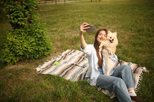 Caucasian girl student female pet owner taking selfie photo with dog, image on smart phone, having video call conversation with dog online in park