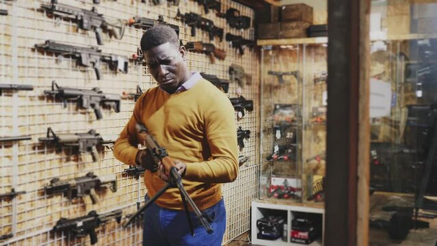 African-american man choosing machine gun in air weapon shop.