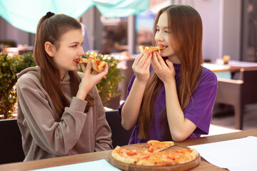 two teen girls eating pizza in cafe outdoors after study in classes. Two Friends Sharing Pizza...