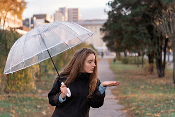 Portrait of young woman with long brown hair standing outside and holding umbrella. Girl with an umbrella on cloudy autumn day.