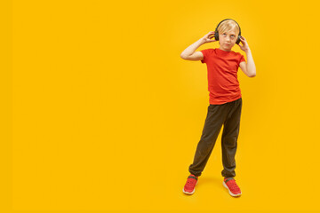 Full-length portrait of schoolboy in headphones, in isolation on yellow background. Teenage child listens to music. Copy space.