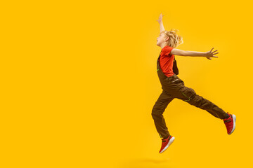Fototapeta na wymiar Side view full-length portrait of bouncing boy on yellow background. Child jumps happily. Copy space, place for text