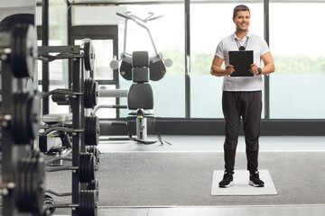 Fototapeta na wymiar Full length portrait of a sports coach holding a clipboard and smiling in a gym