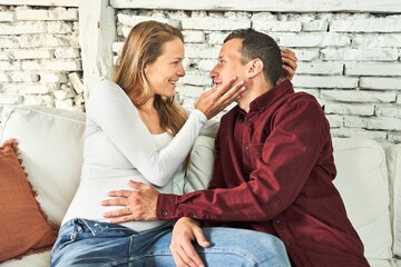 A blissful couple, both 40, expecting a baby, radiates joy on their cozy sofa at home.