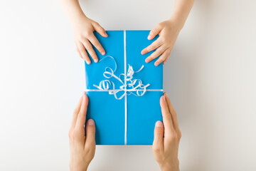 Mother hands giving big blue wrapped gift box to baby boy on white table background. Closeup. Point of view shot. Children congratulation concept. Top down view.