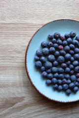 Turquoise plate with fresh blueberries on wooden background. Top view.