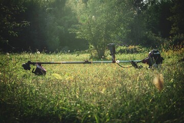 Brush cutter at outdoors against a background of a green garden with trees