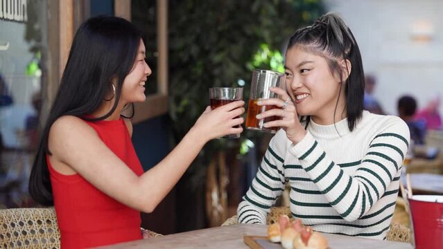 Slow motion of happy Asian women clinking glasses of cold tea in cafe