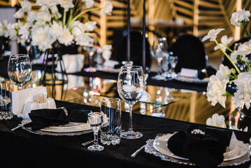 Festive decor with flower composition, candles on black tablecloth. Banquet decoration in hall restaurant. Wedding setup, dinner table reception in area on party. Setting. Birthday, baptism, event.