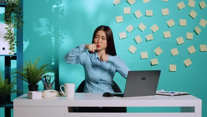 Happy playful asian office worker having fun pretending to fight, throwing punches. Funny high spirited businesswoman mock boxing in relaxed colourful workplace over blue studio background - Powered by Adobe