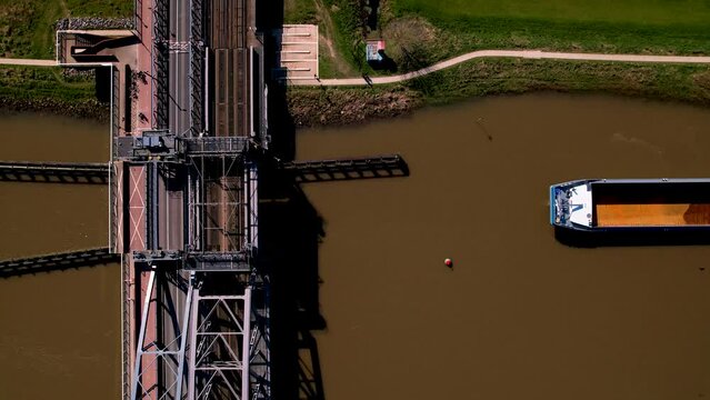Time lapse of empty cargo ship navigate upstream on river IJssel and sailing passed steel draw bridge passageway. Inland shipping raw material marine transport top down aerial.