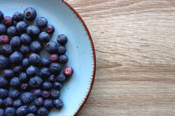 Turquoise plate with fresh blueberries on wooden background. Top view.