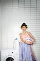 asian young woman with hair curlers standing in pink ruffled top, pearl necklace and tulle skirt...