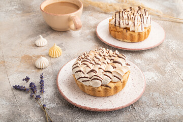 Two tartlets with meringue cream and cup of coffee on brown concrete, side view.