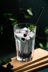 Vertical shot of a lemonade with ice and blackberry on a wooden board on the blurred background