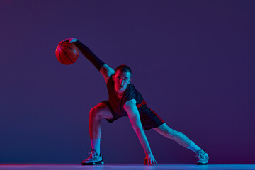 Concentration and motivation. Young man, basketball player in motion with ball against purple...
