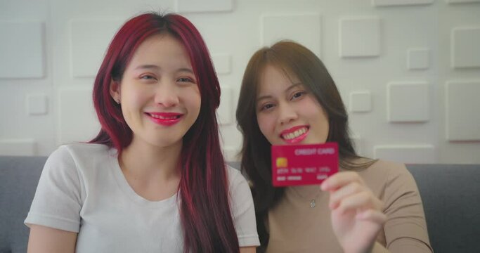 Two asian woman holding credit card with smile. They looking to camera with smiling together in living room.
