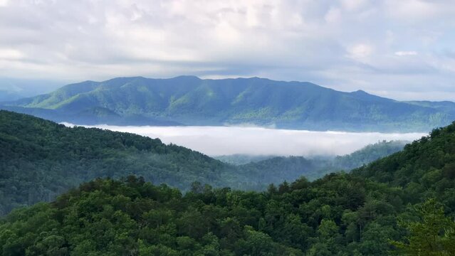 Time lapse scene of white clouds moving on green smoky mountains range