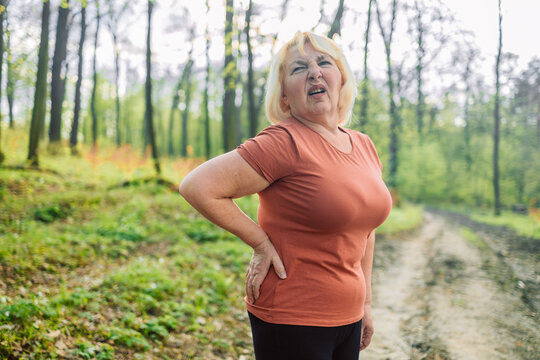 Tired senior 50s 60s athlete runner exhausted of cardio workout breathing hard after difficult exercise in a park. Caucasian fitness woman running s muscle back pain or cramps. High quality photo