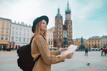 Upset stylish clothes blond girl tourist travels looking for directions on map while traveling through the old town of Krakow in spring, Poland. St. Marys Basilica. High quality photo