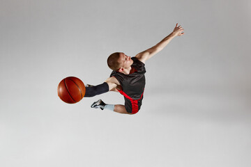 Dynamic image of male basketball player in motion, jumping with ball against grey studio background. Top view. Slam dunk. Concept of professional sport, healthy lifestyle, action and motion © master1305