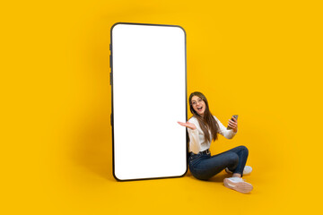 Woman demonstrate big empty screen smartphone mockup. Great mobile offer, application concept idea image. Caucasian excited smiling attractive girl sitting near big huge mobile phone. Copy space. - Powered by Adobe