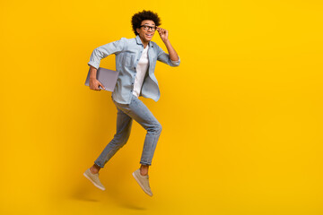 Fototapeta na wymiar Full length profile portrait of cheerful handsome guy hold netbook run jump empty space isolated on yellow color background