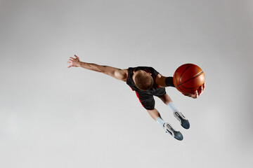 Motivated sportsman, male basketball player in motion, jumping with ball against grey studio...