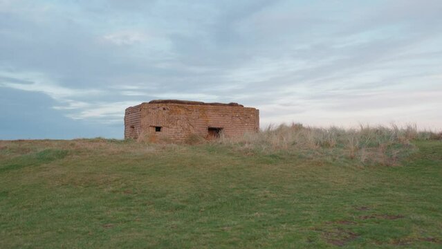 Fixed establishing clip of historic world war shelter on the English coastline at sunset.