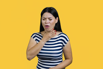 Asian woman having morning sickness feeling nausea and want to vomit. Young korean lady is coughing. Isolated on yellow background.