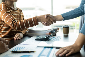 A successful Asian woman with a partner shakes hands at the office after the project is completed, the concept workers meeting shakes hands.