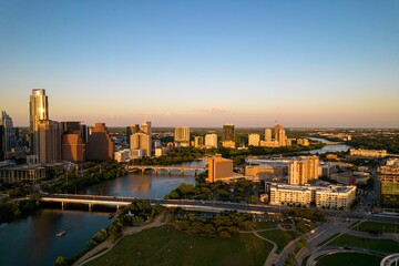 Drone shot of TX skyline with waterfront, greenery and blue sky at sunset in Austin city