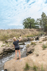 Naklejka premium Adventurer woman taking selfies with mobile phone outdoors near a water stream.